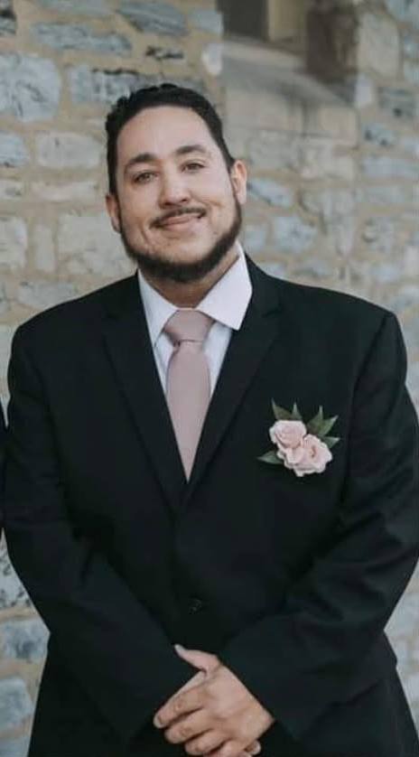 DJ Angel in a black suit with a pink tie and boutonniere