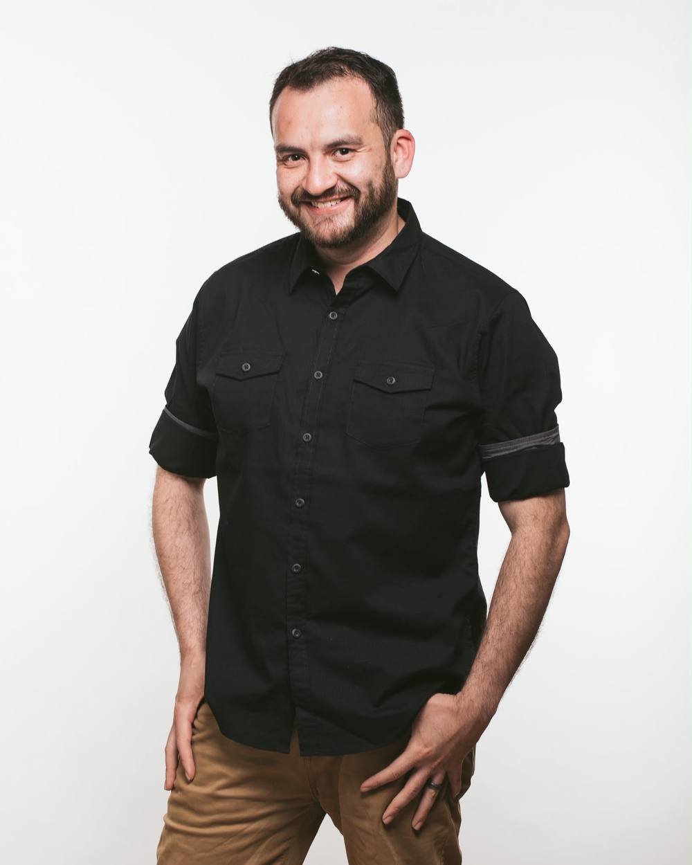 DJ Bash smiling in a black shirt, studio portrait