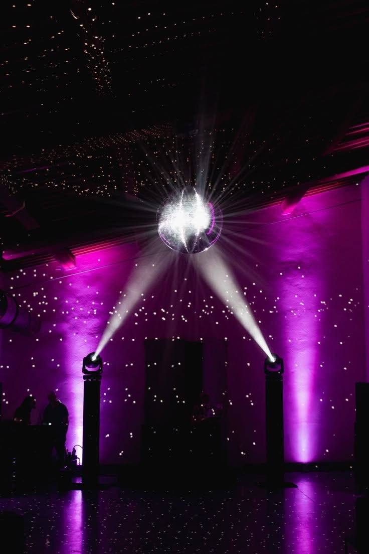 Moving-head lights sending beams onto a mirror ball over a purple-lit dance floor