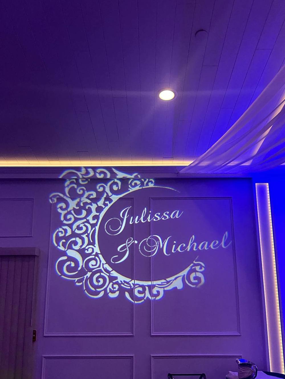 Custom monogram with the couple’s names projected on a wall in purple light